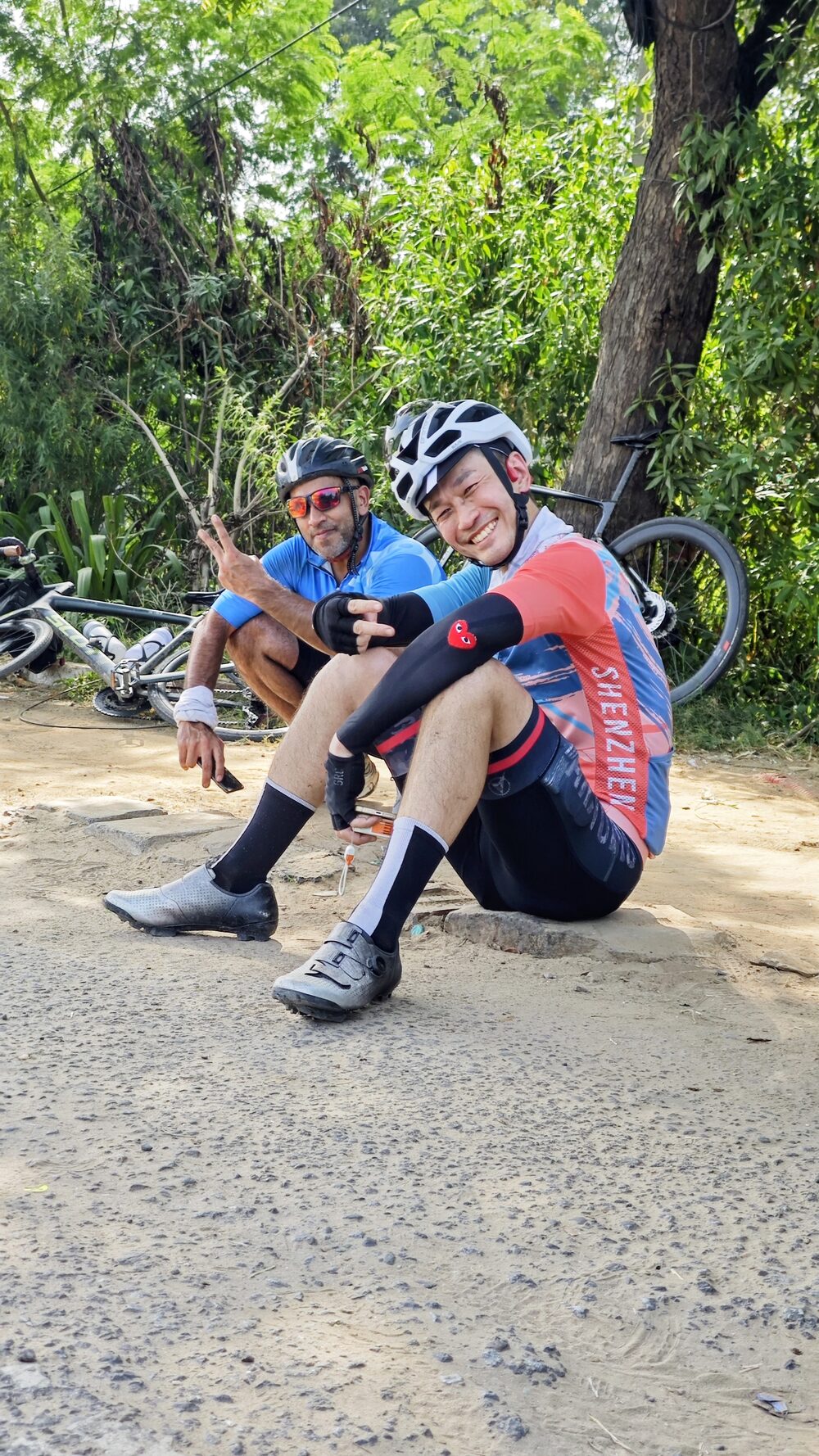 A cyclist sitting on the gravel at the roadside, taking a break